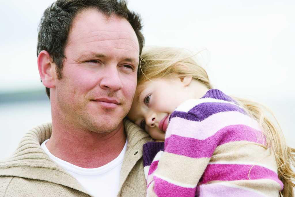 A close up image of a father holding his daughter in his arms at the beach.