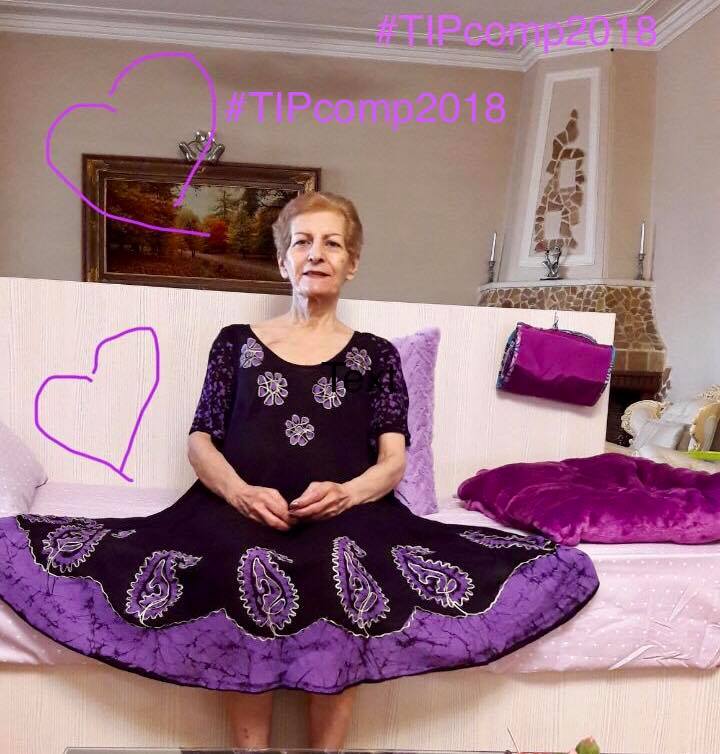 Lady sat on sofa in a purple floral dress with text "#TIPcomp2018" handwritten on image