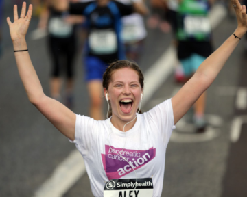 Woman wearing a PCA branded t-shirt celebrates completing a running event