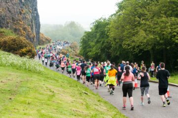 Large crowd of runners ascending a foggy green hill near Edinburg